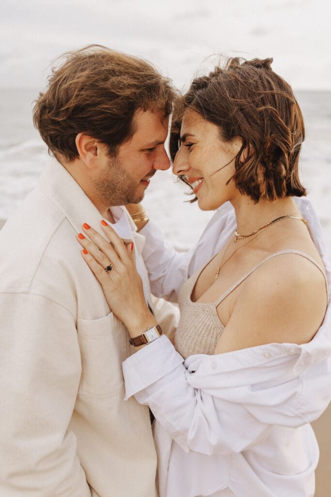 Futurs parents qui rient ensemble sur la plage, séance grossesse naturelle et authentique